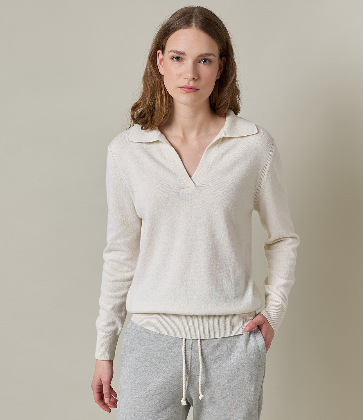 A woman wearing a beige V-neck sweater with long sleeves, paired with gray pants. The image captures a casual, relaxed style suitable for everyday wear.