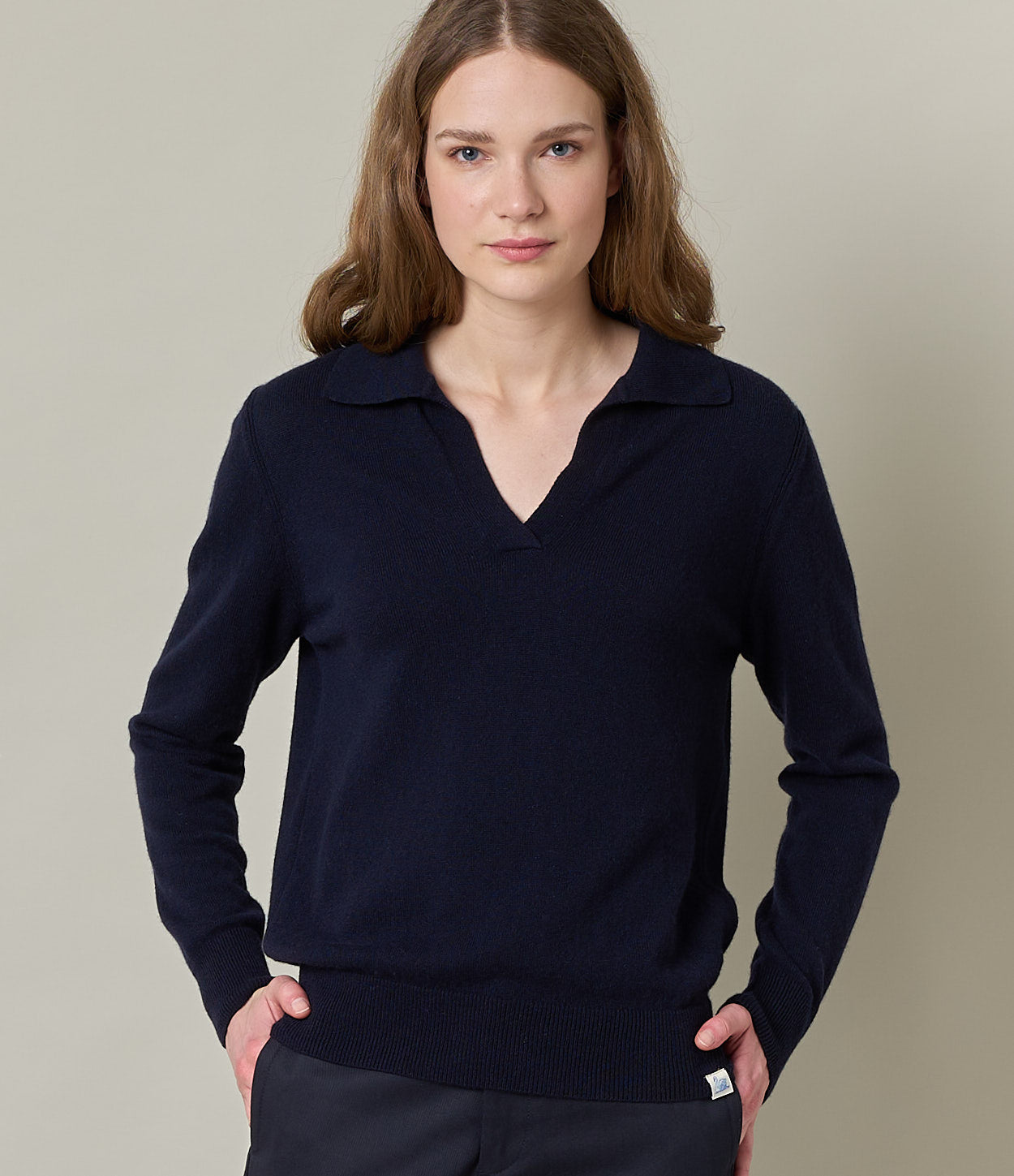 A person wearing a navy blue V-neck sweater with long sleeves, paired with dark pants. The sweater has a knitted collar and appears to be made of a blend of merino wool, cashmere, and silk.