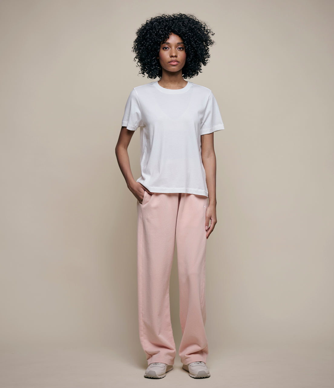 Person wearing a white t-shirt and pink pants against a beige background