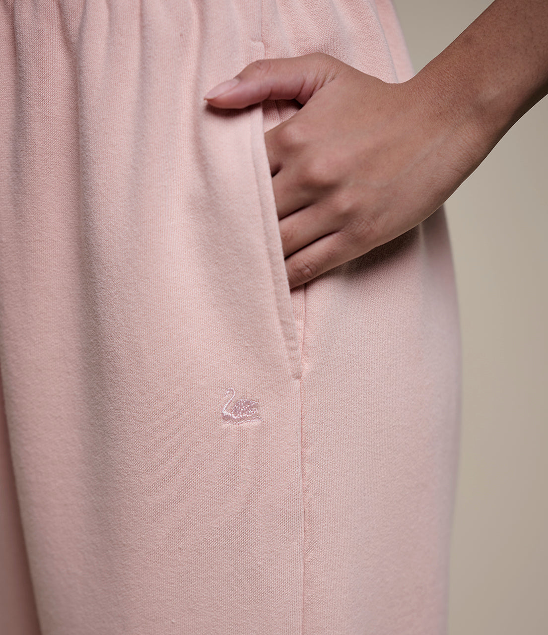 Close-up of a light pink garment with a brand logo, held by a hand against a neutral background.