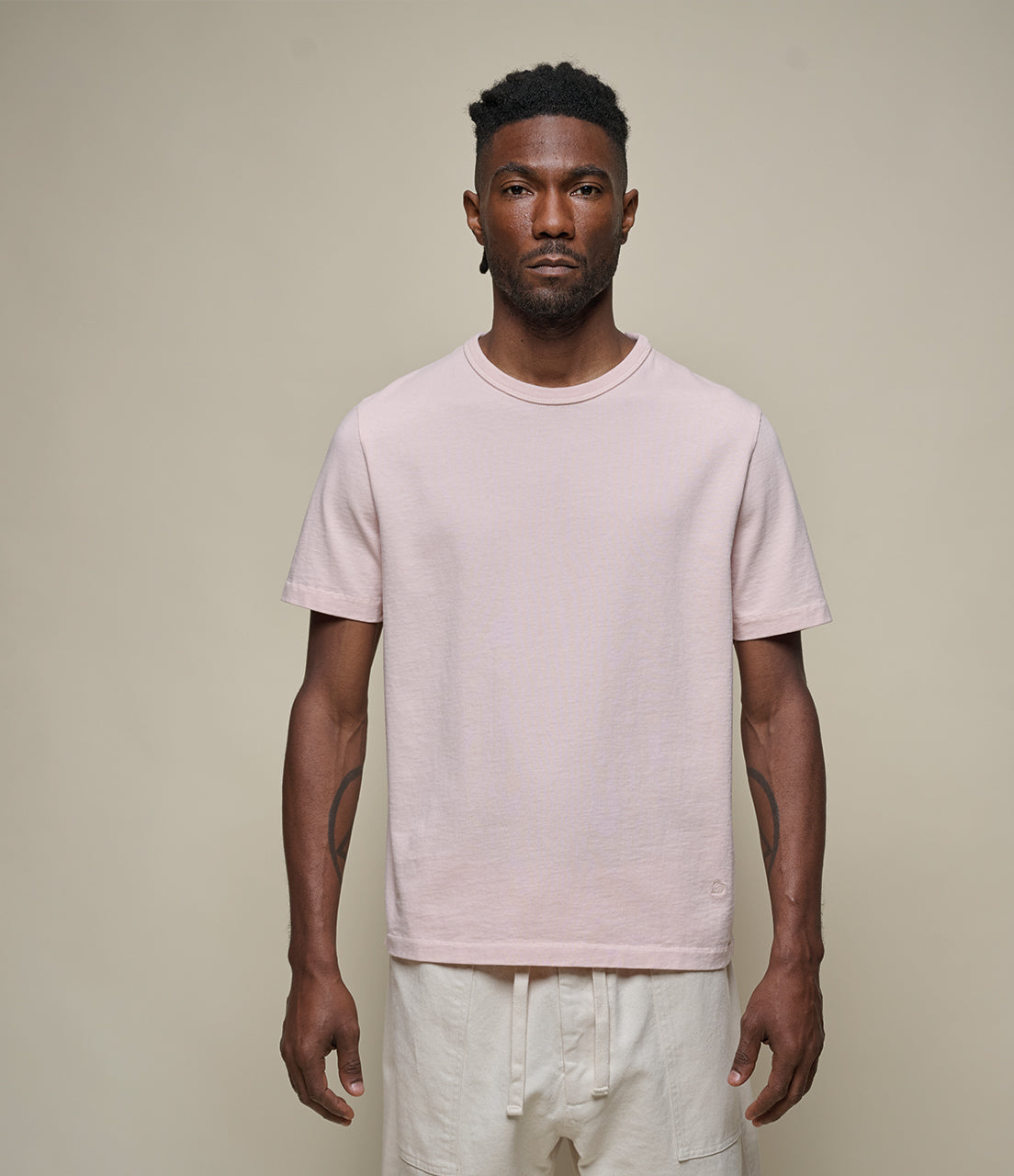 Man wearing a light pink t-shirt and white pants against a beige background