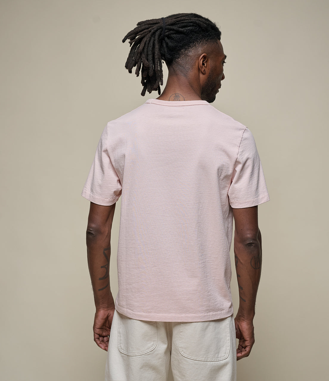 Man wearing a light pink t-shirt and light-colored pants against a beige background