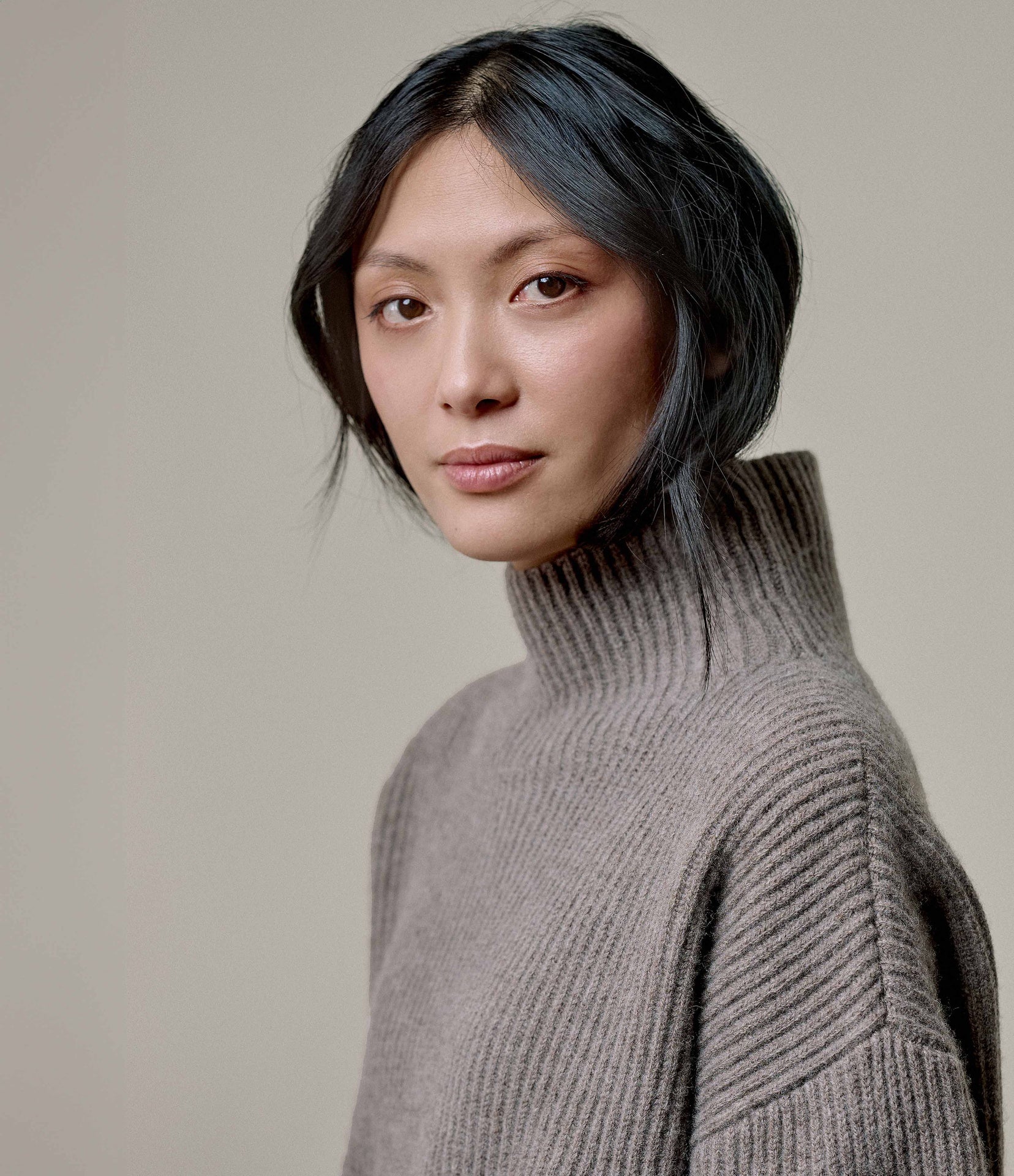 Person wearing a gray turtleneck sweater against a plain background