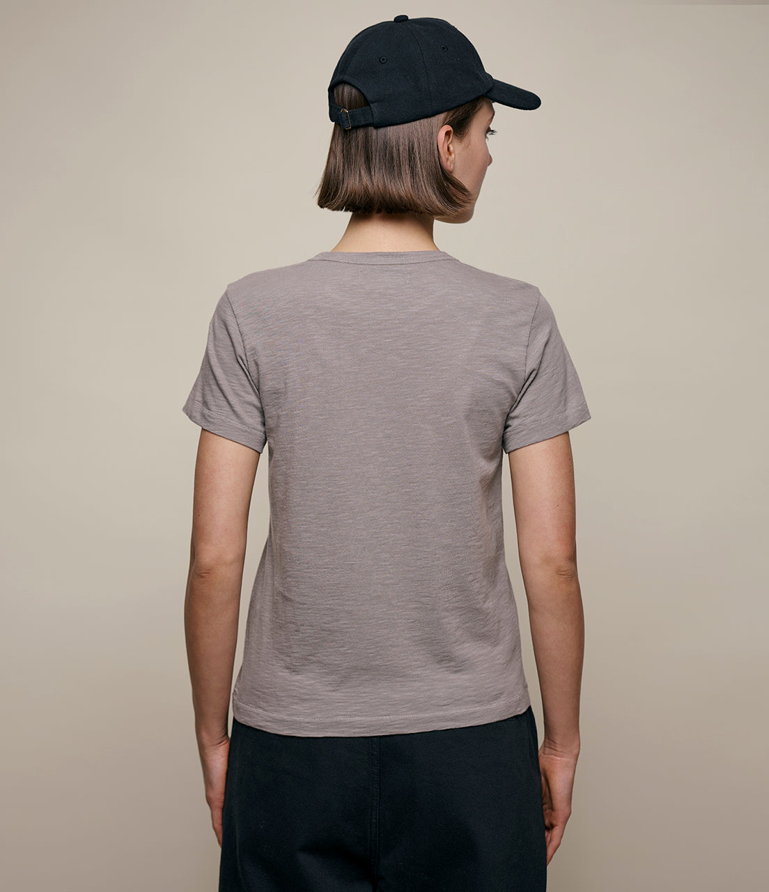 Person wearing a gray t-shirt and black cap on a beige background