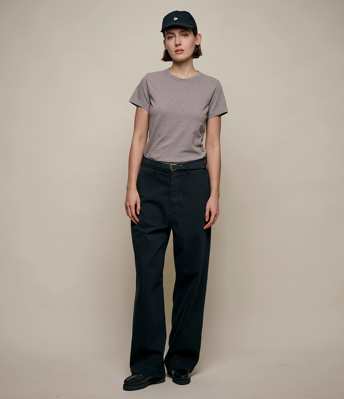 Person wearing a gray t-shirt and black pants against a beige background