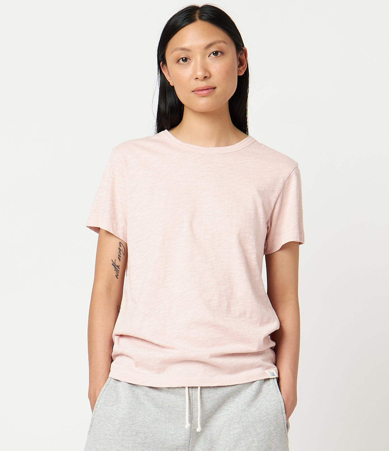A woman wearing a light pink, short-sleeved T-shirt with a round neckline.