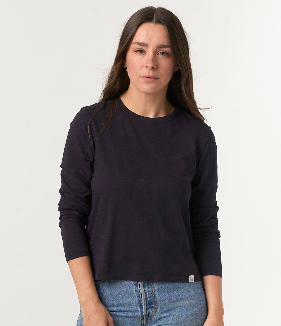A woman wearing a navy longsleeve t-shirt made of PIMA cotton, paired with blue jeans.