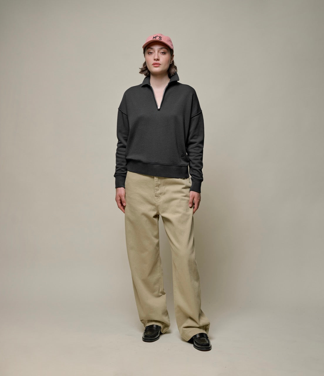 Person wearing dark grey halz zip sweatshirt, khaki pants and a pink cap