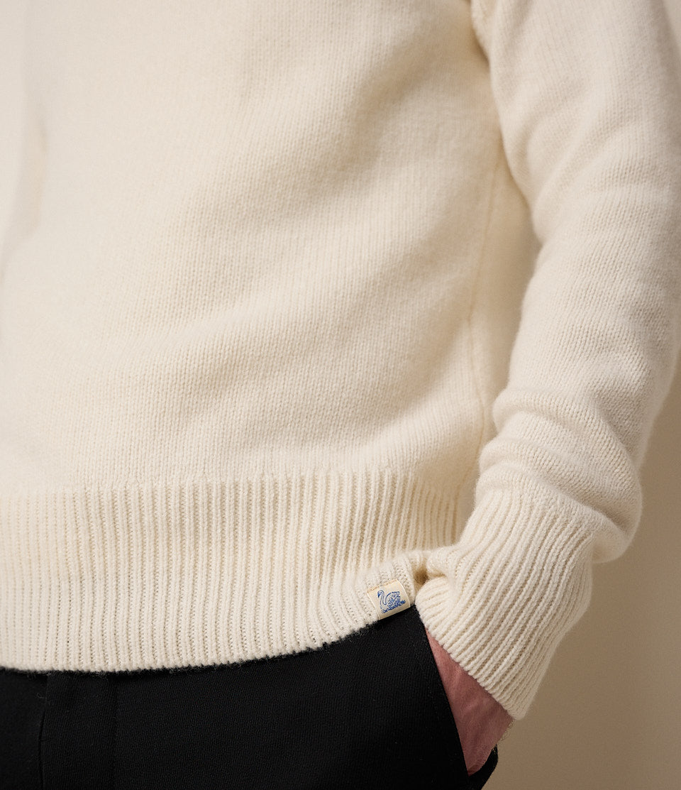 Close-up of a person wearing a cream sweater with a visible brand logo.