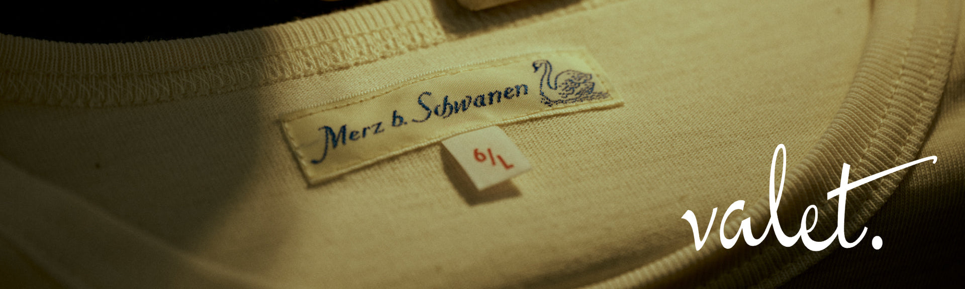 Close-up of an olive green garment tag reading Merz b. Schwanen, next to the valet. logo