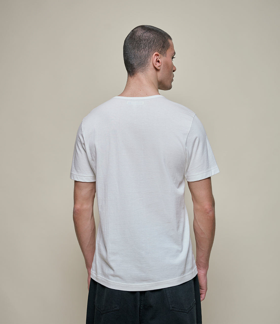 Man wearing a plain white t-shirt against a beige background