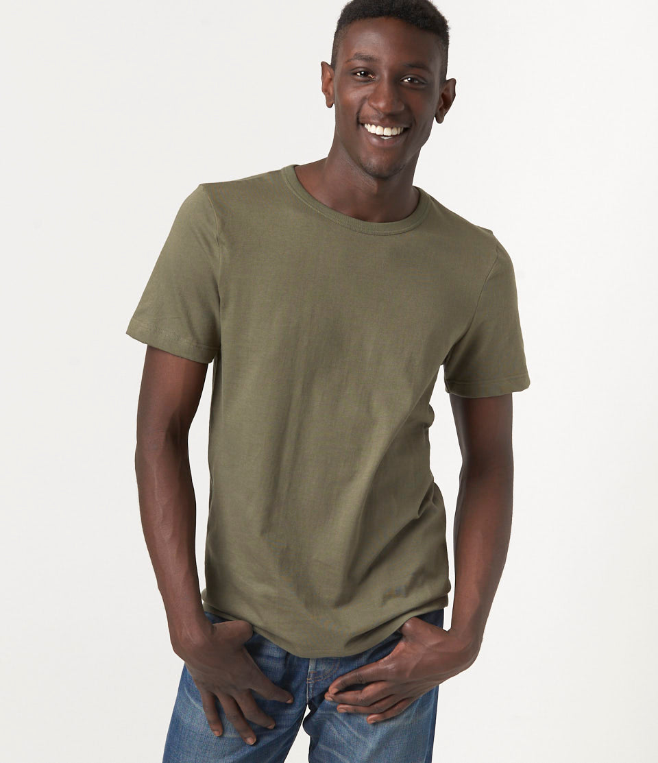 A man wearing a green, loopwheeled short-sleeved, round-neck T-shirt and blue jeans.