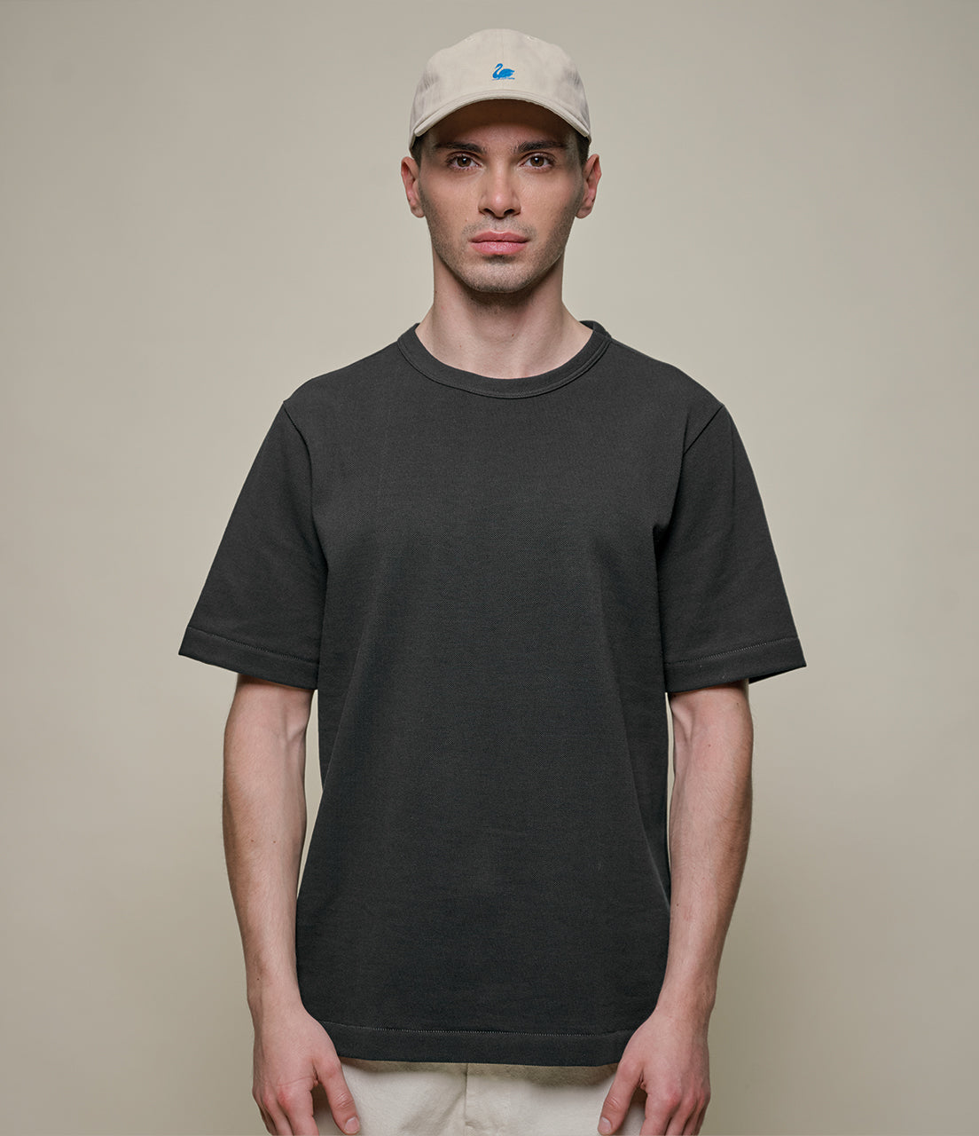 Man wearing a black t-shirt and beige cap against a plain background