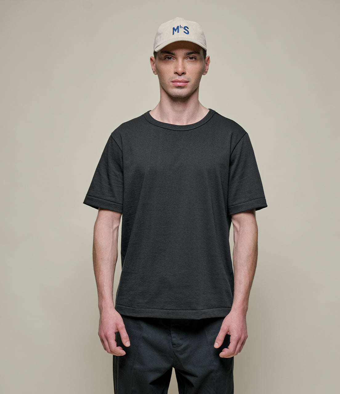 Man wearing a black t-shirt and beige cap on a plain background