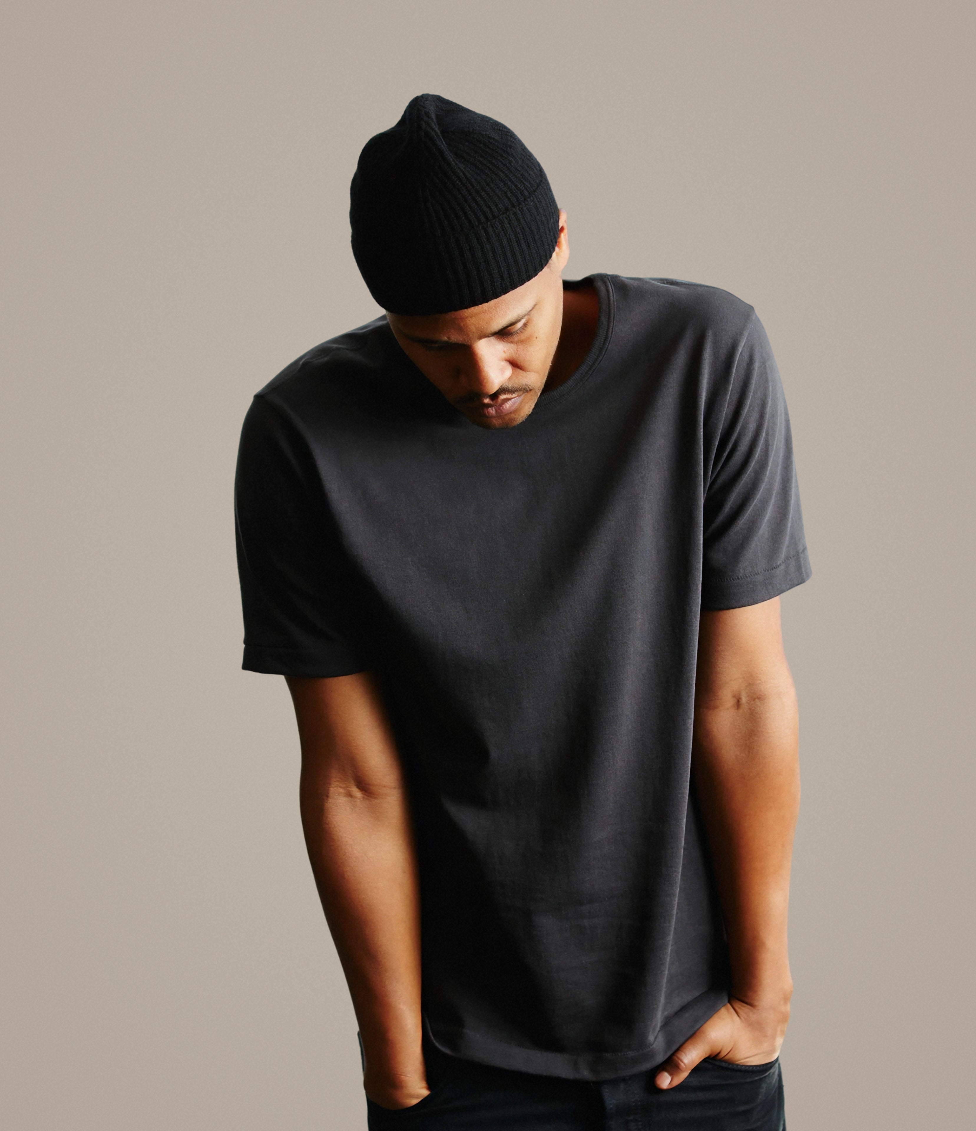 Man wearing a dark gray t-shirt and black beanie against a neutral background