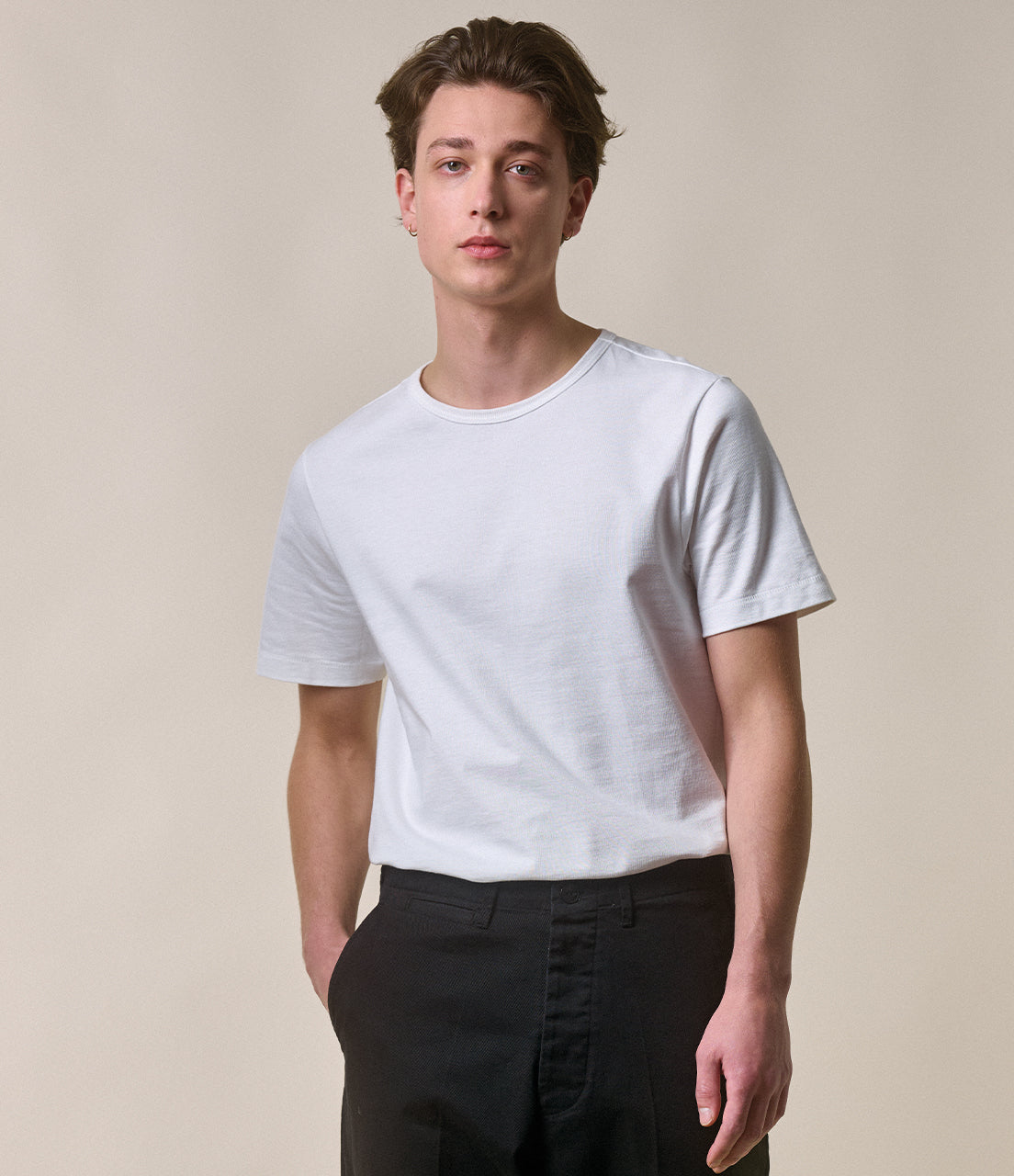 Man wearing a plain white t-shirt and black pants against a beige background