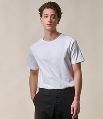 Man wearing a plain white t-shirt and black pants against a beige background