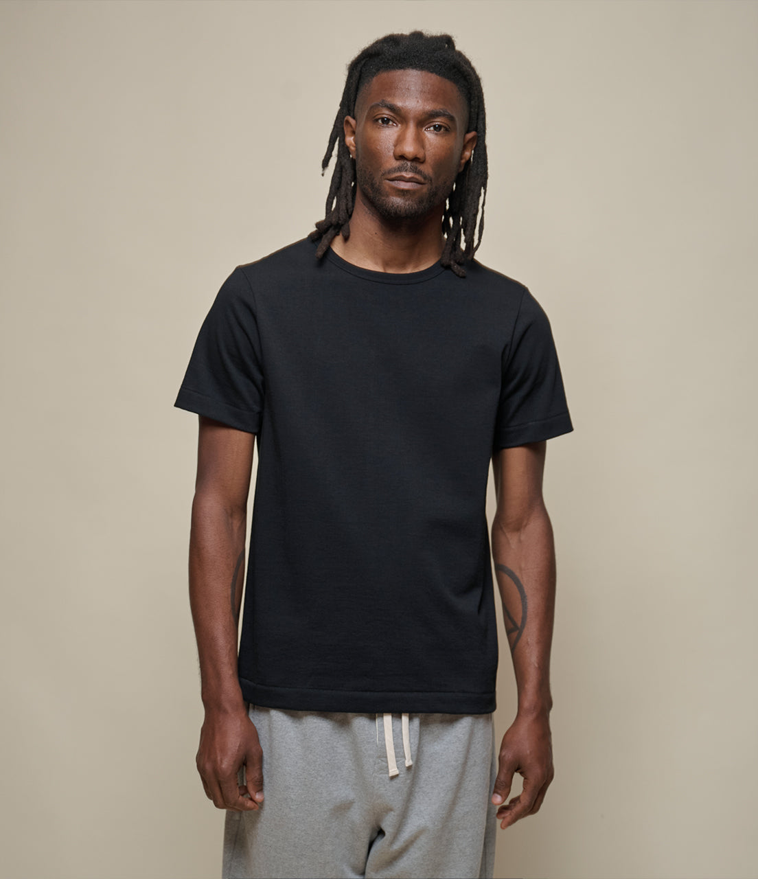 Man wearing a black t-shirt and gray pants against a beige background