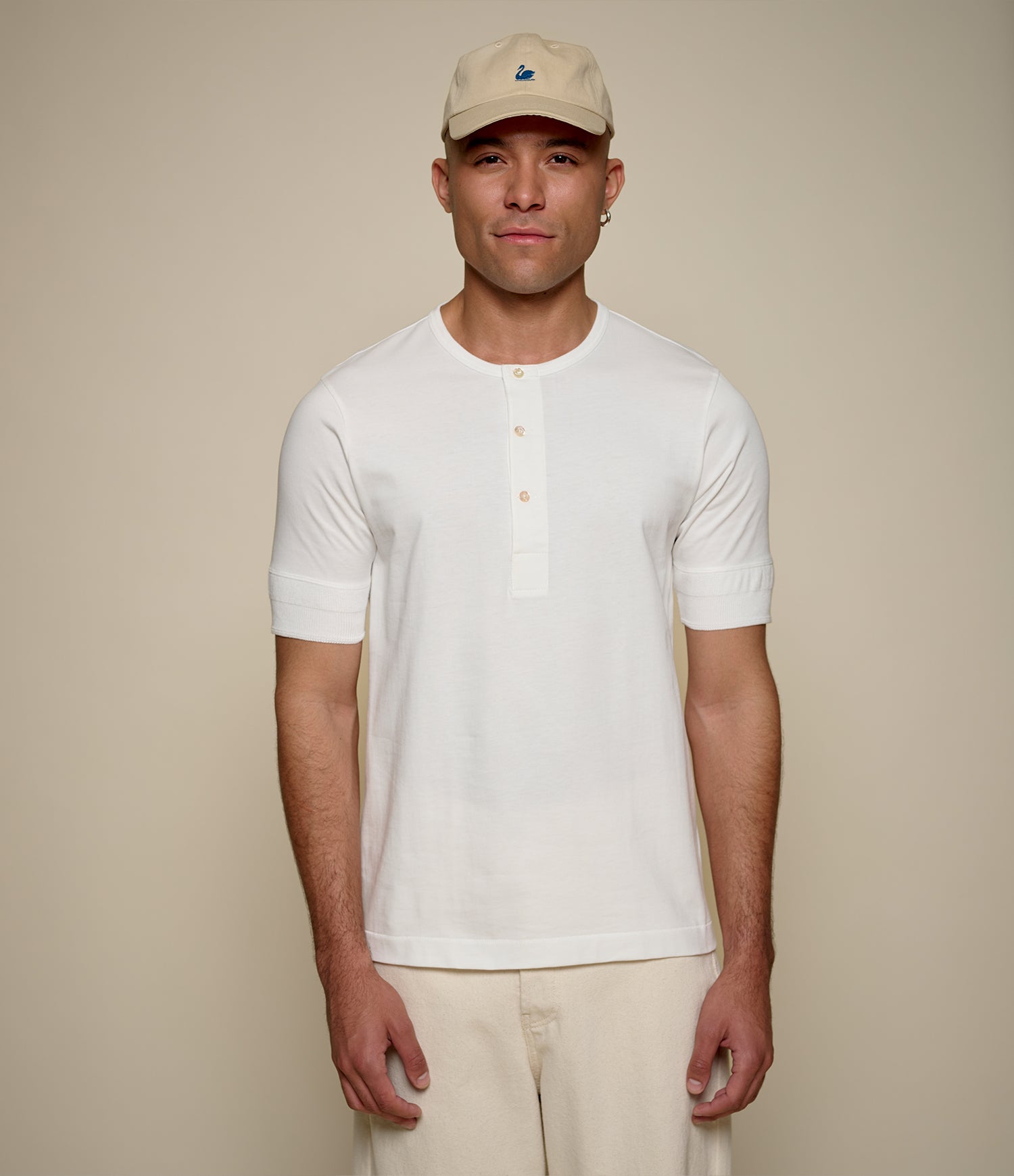 Man wearing a white henley shirt and beige cap against a plain background