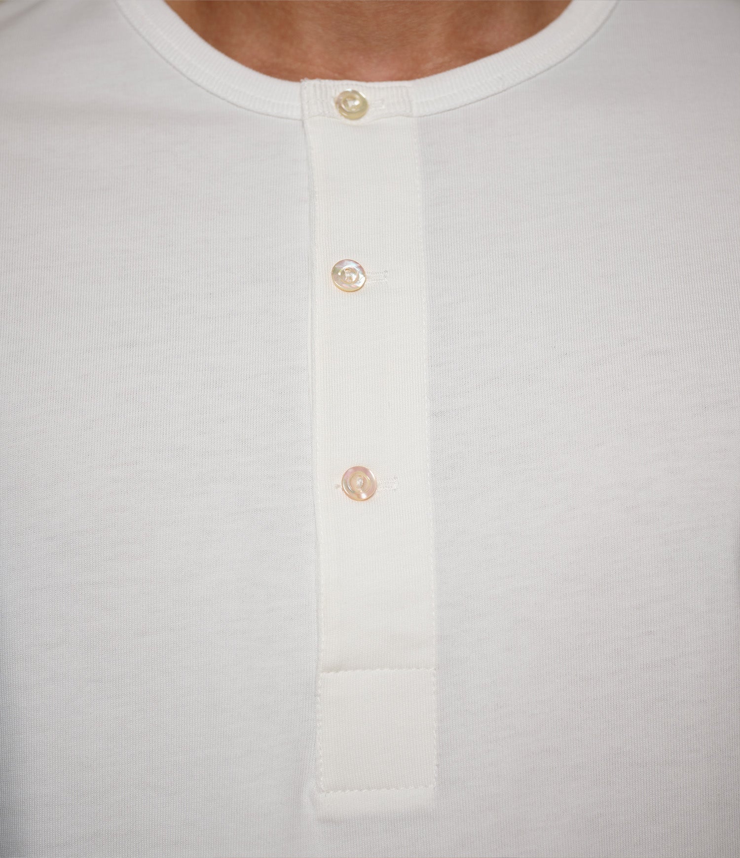Close-up of a white henley shirt with button details on a light gray background