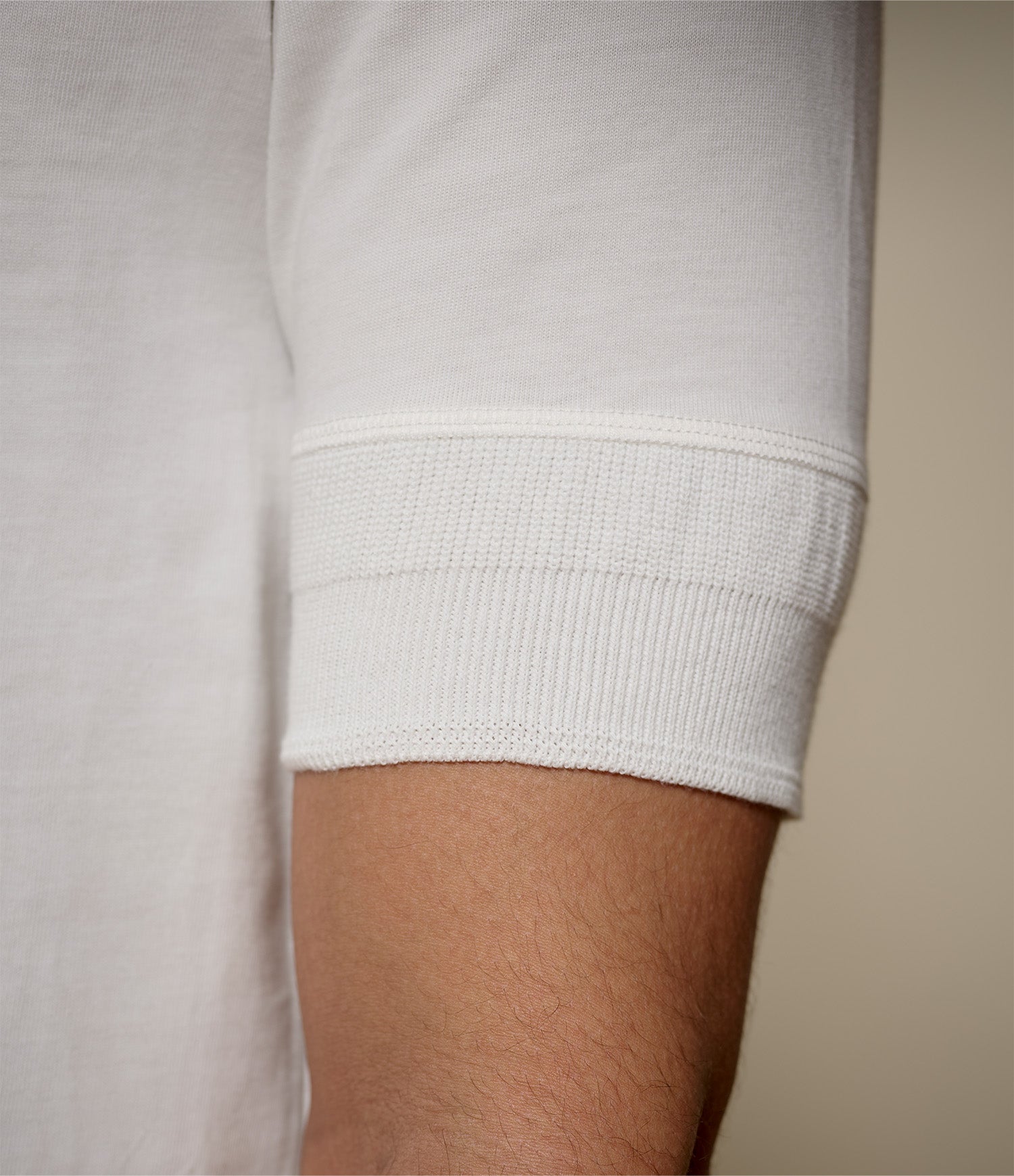 Close-up of a person wearing a white henley with cuffs on the sleeves against a neutral background