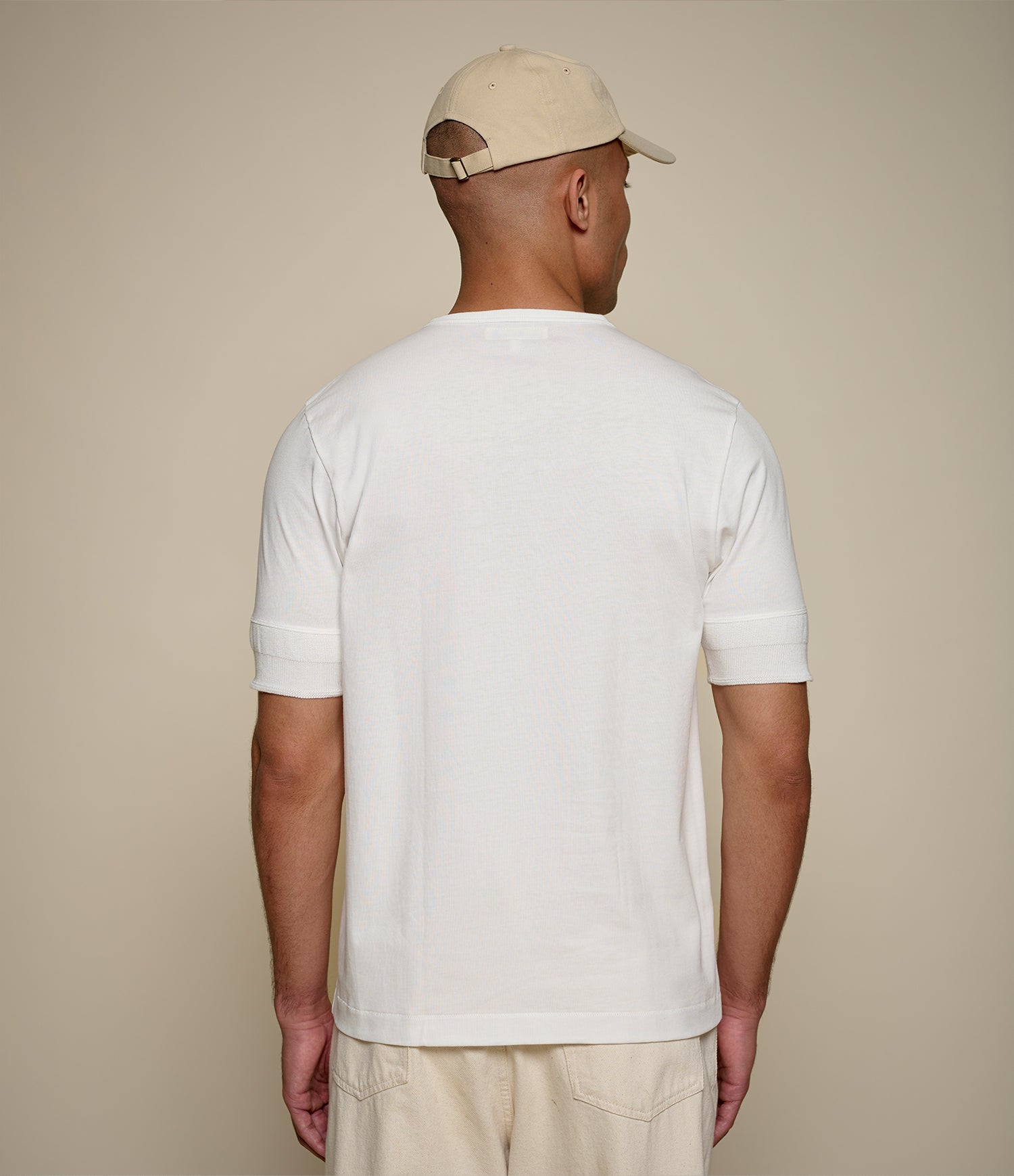 Man wearing a plain white henley and beige cap against a beige background