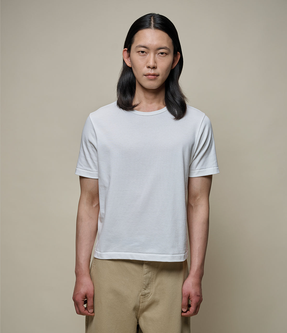 Person wearing a plain white cropped t-shirt and beige pants against a neutral background