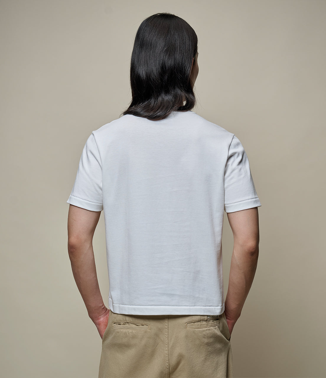 Person wearing a plain white cropped t-shirt and beige pants against a beige background