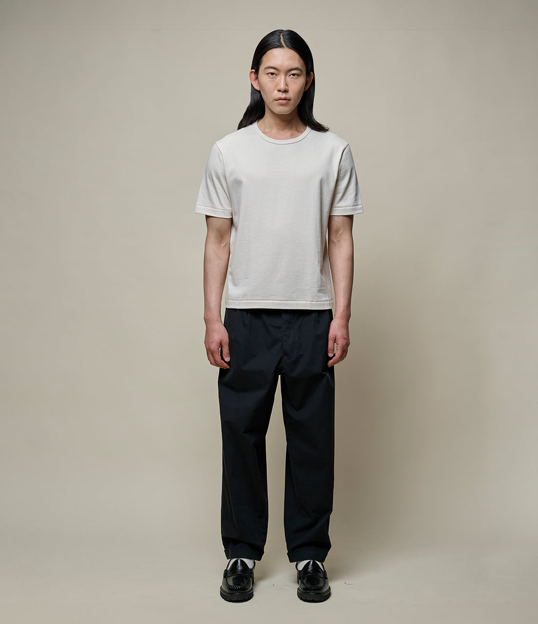 Person wearing a beige cropped t-shirt and black pants against a neutral background