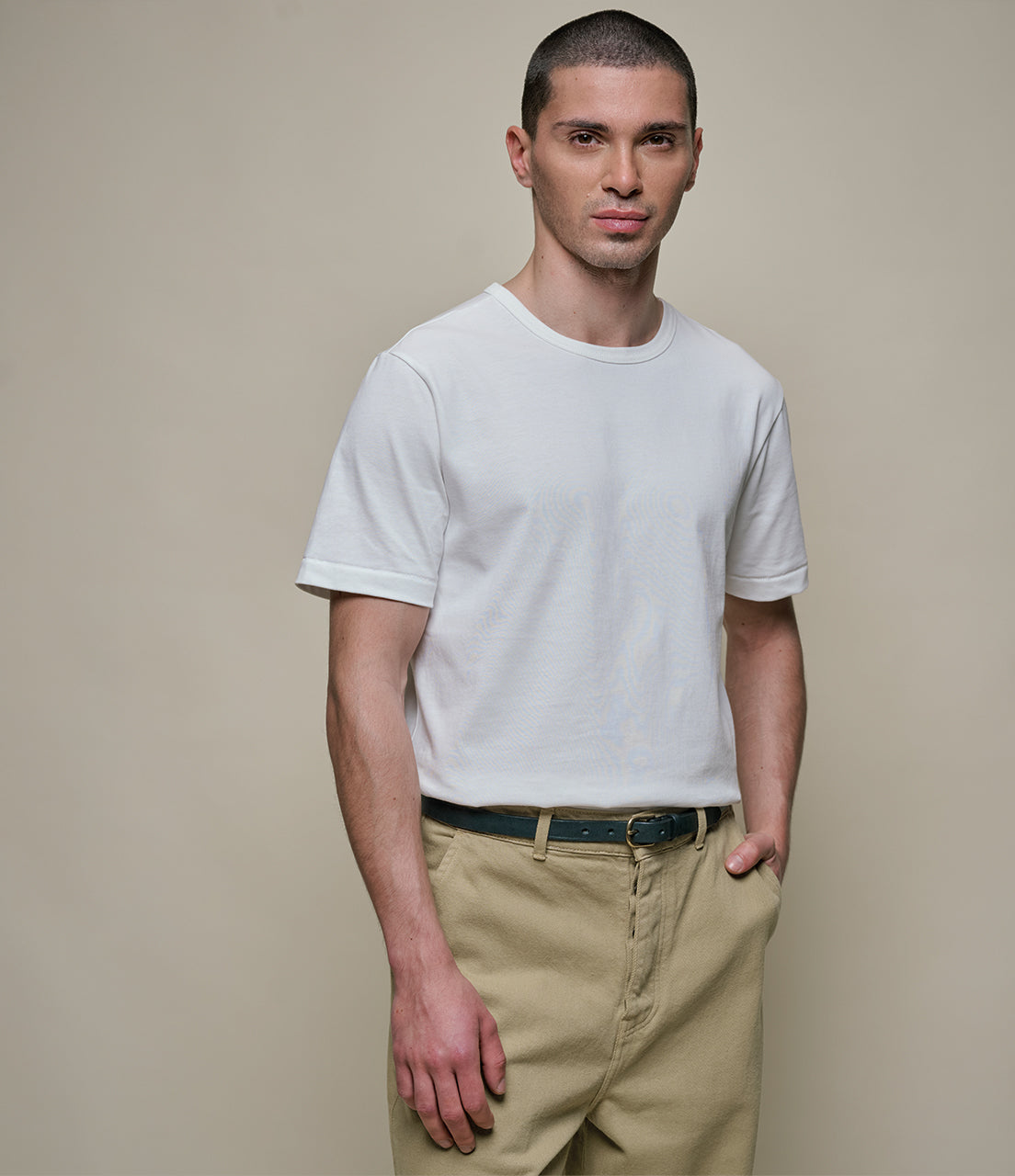 Man wearing a plain white t-shirt and beige pants against a neutral background