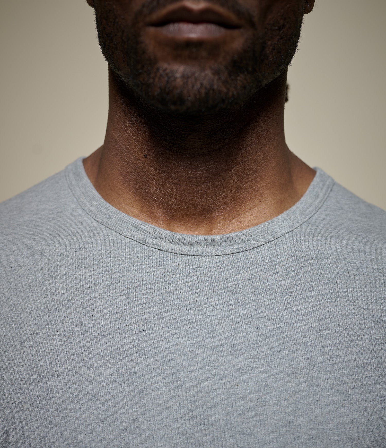 Close-up of a person wearing a gray crew neck t-shirt against a beige background