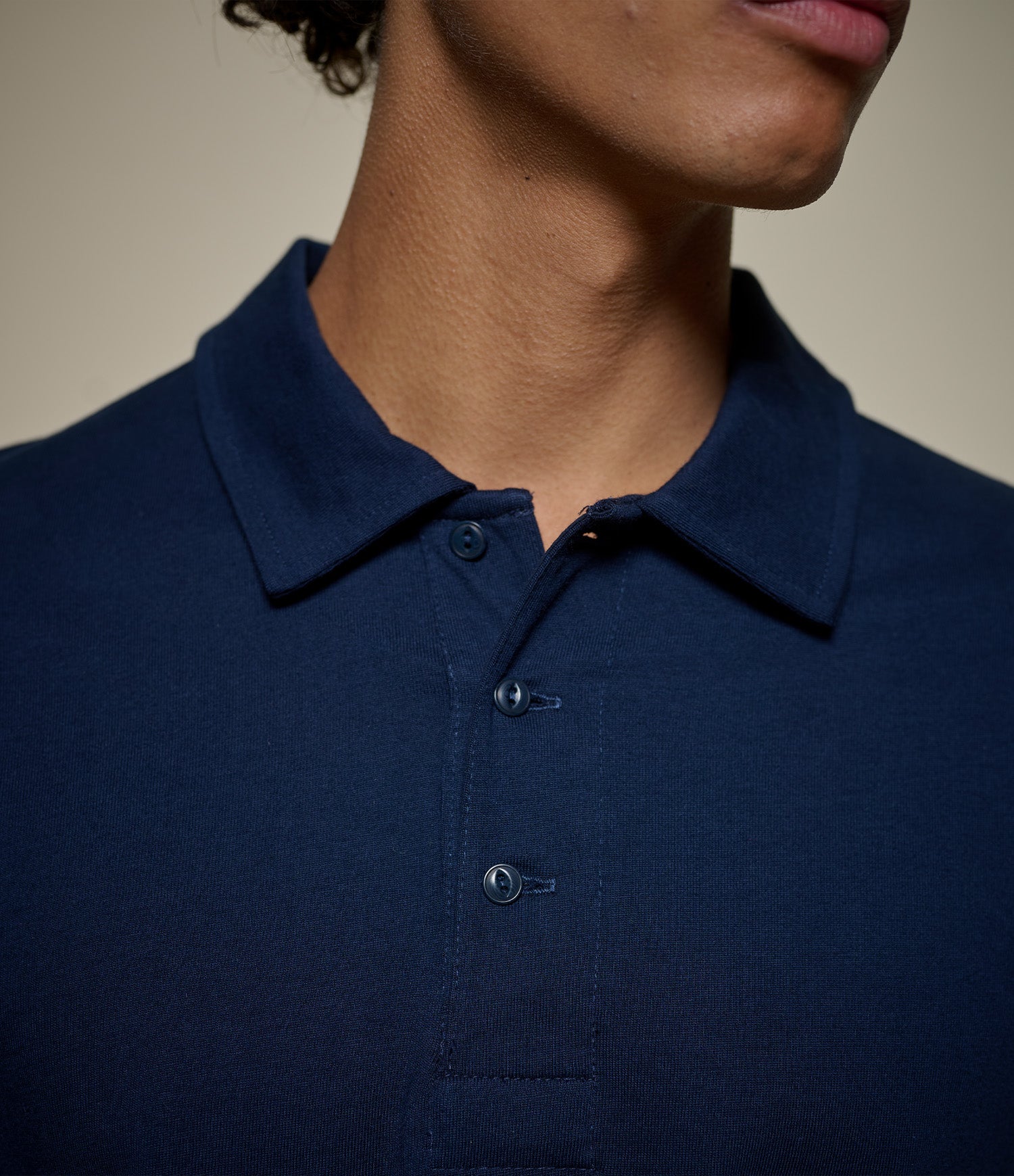 Close-up of a person wearing a dark navy blue polo shirt, showing the collar, buttons, and upper chest against a plain beige background.