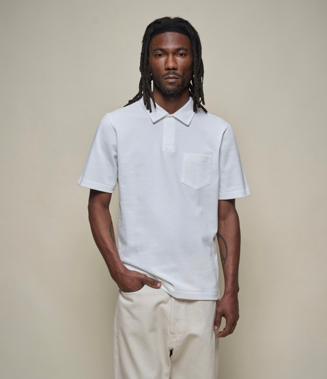 A person wearing a white short sleeve polo shirt with a collar, a front pocket, and light beige trousers.