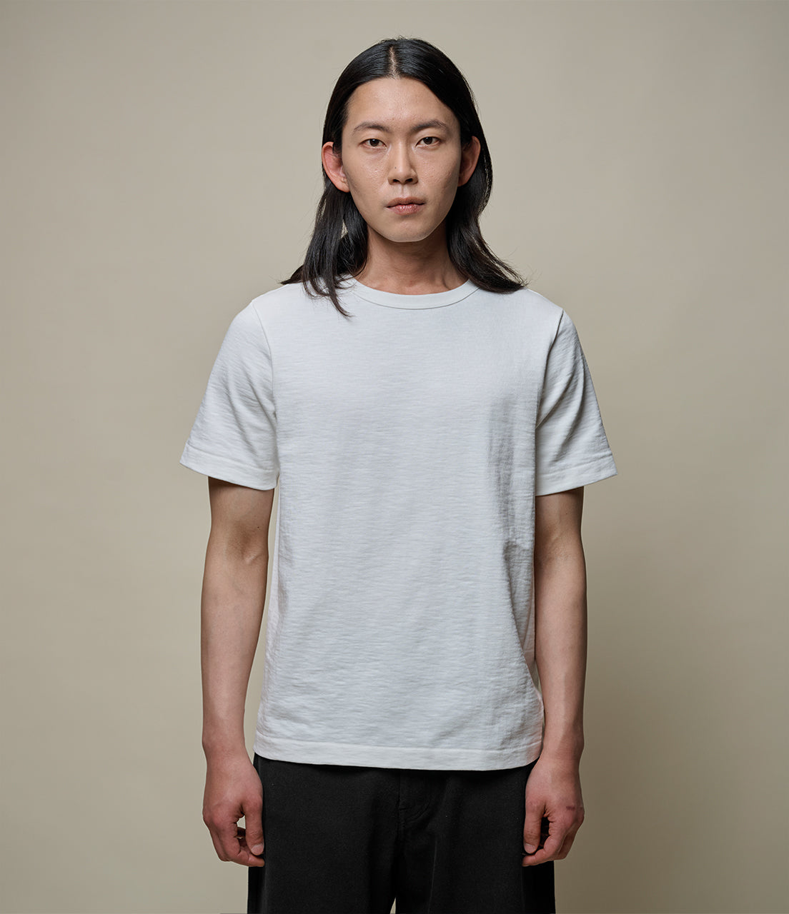 Person wearing a plain white t-shirt against a beige background