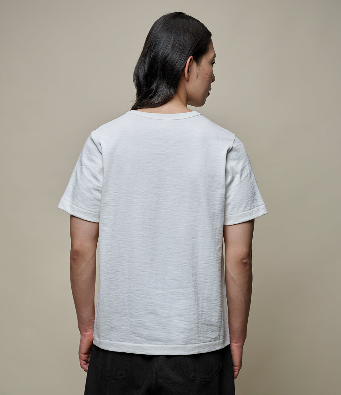 Person wearing a plain white t-shirt against a beige background
