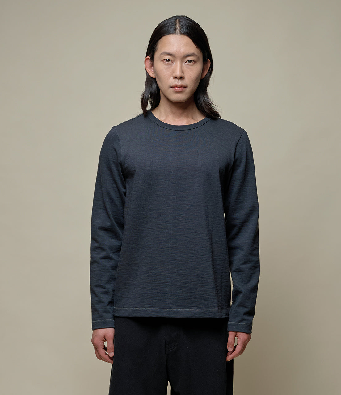 Person wearing a dark gray long-sleeve shirt against a beige background