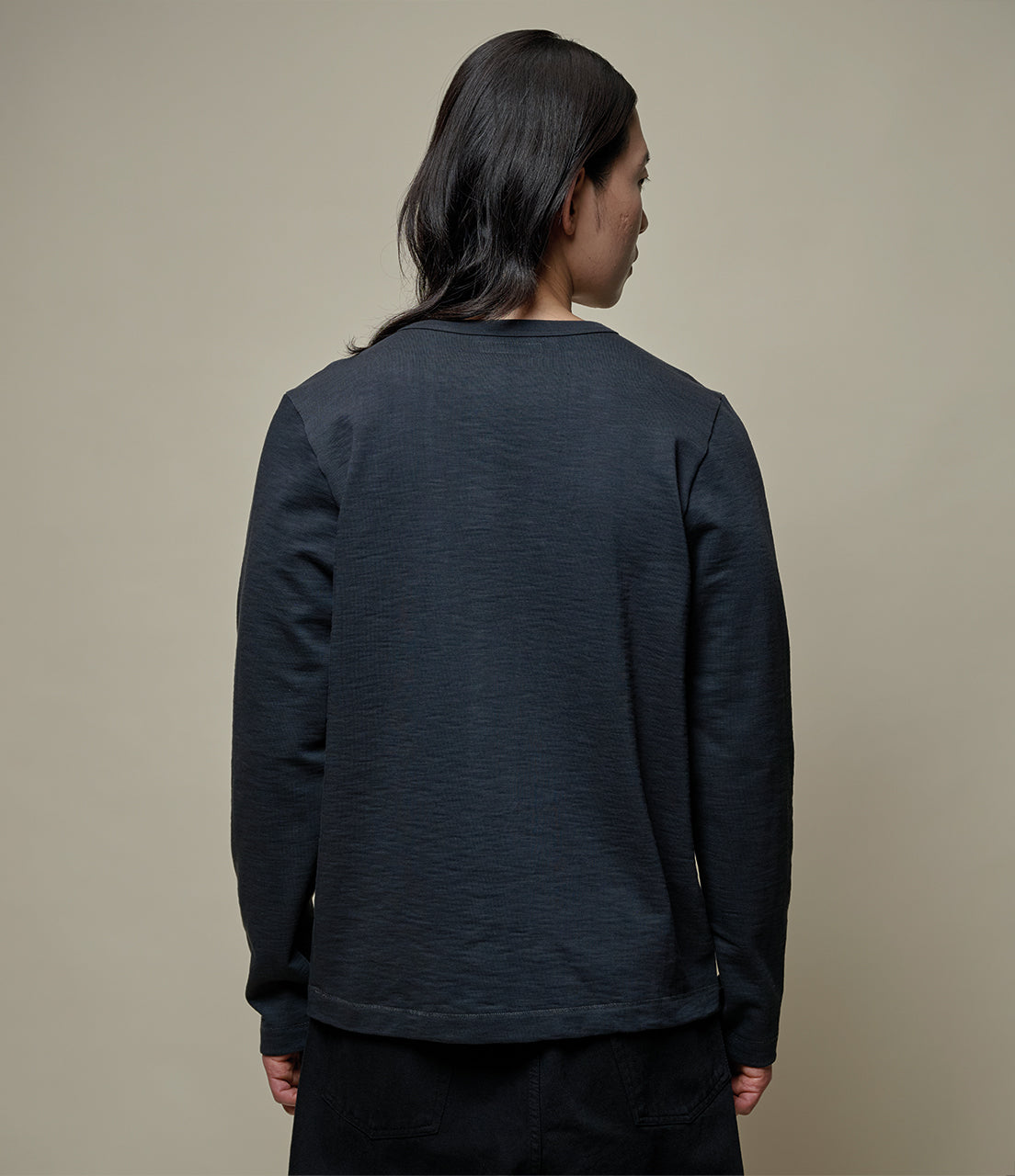 Person wearing a dark gray long-sleeve shirt against a beige background