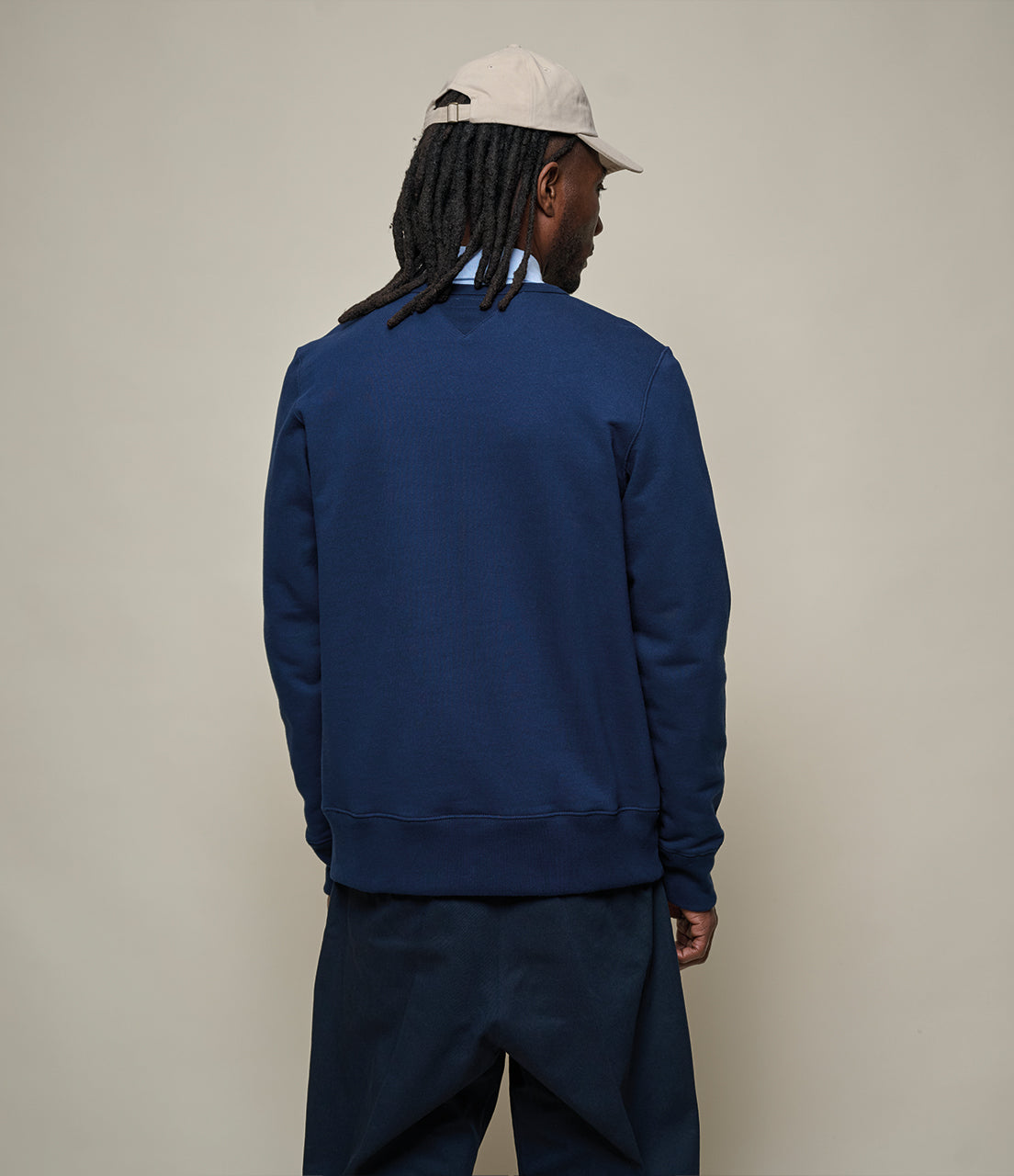 Person wearing a navy blue sweatshirt and pants with a beige cap on a plain background