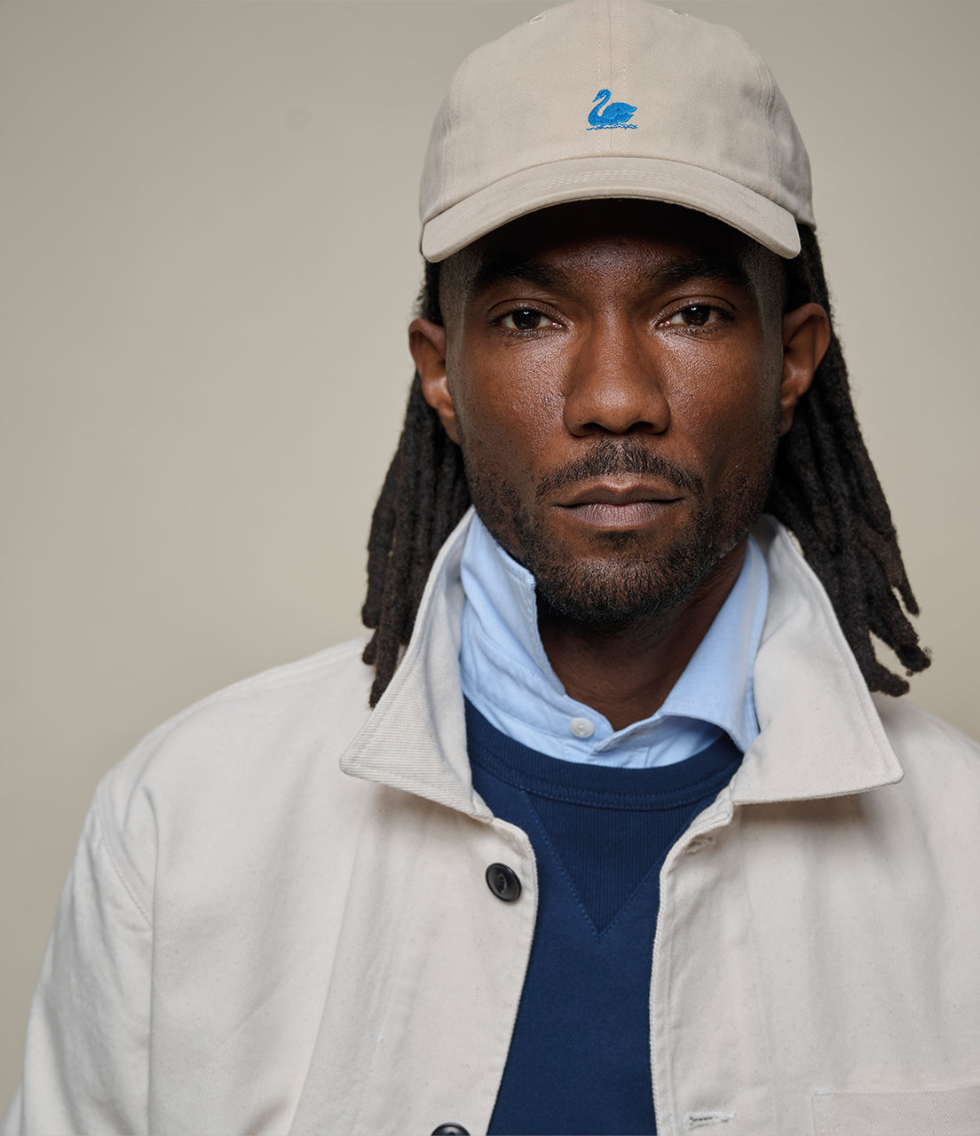 Man wearing a beige cap with a logo, light jacket, and blue shirt against a plain background