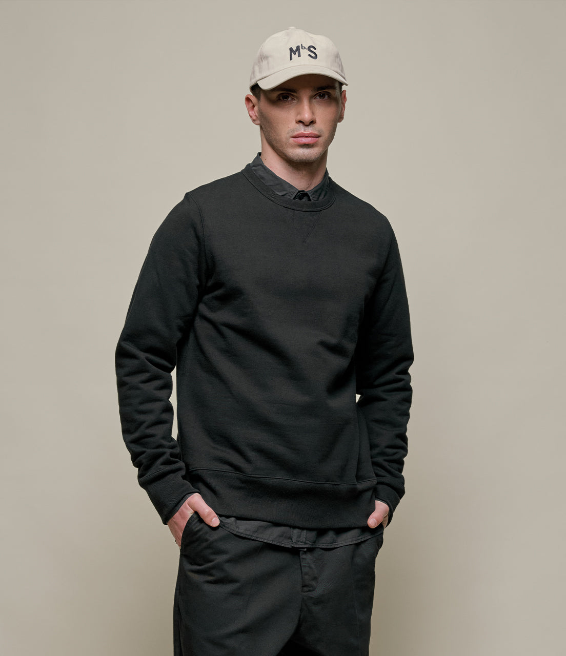 Man wearing a black sweater and beige cap against a plain background