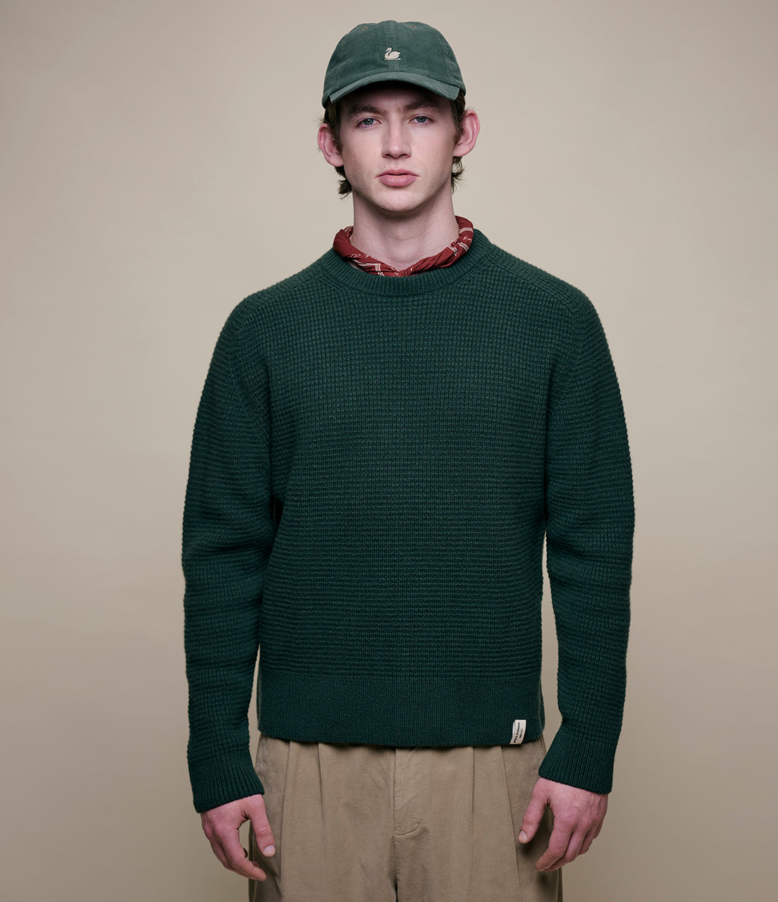 Man wearing a green sweater and cap against a beige background