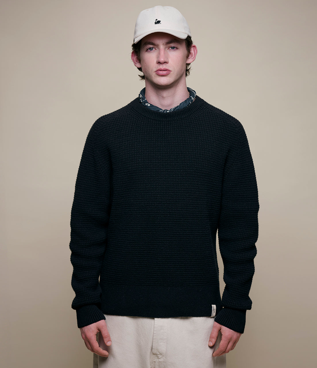 Man wearing a black sweater and beige cap against a beige background