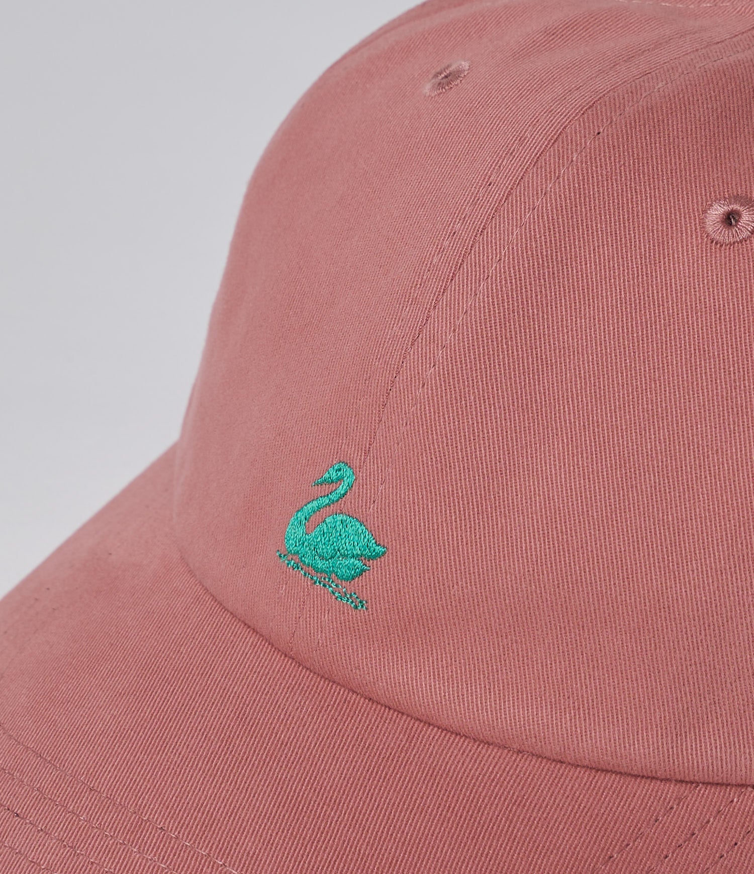 Pink cap with a green embroidered swan design on a light gray background