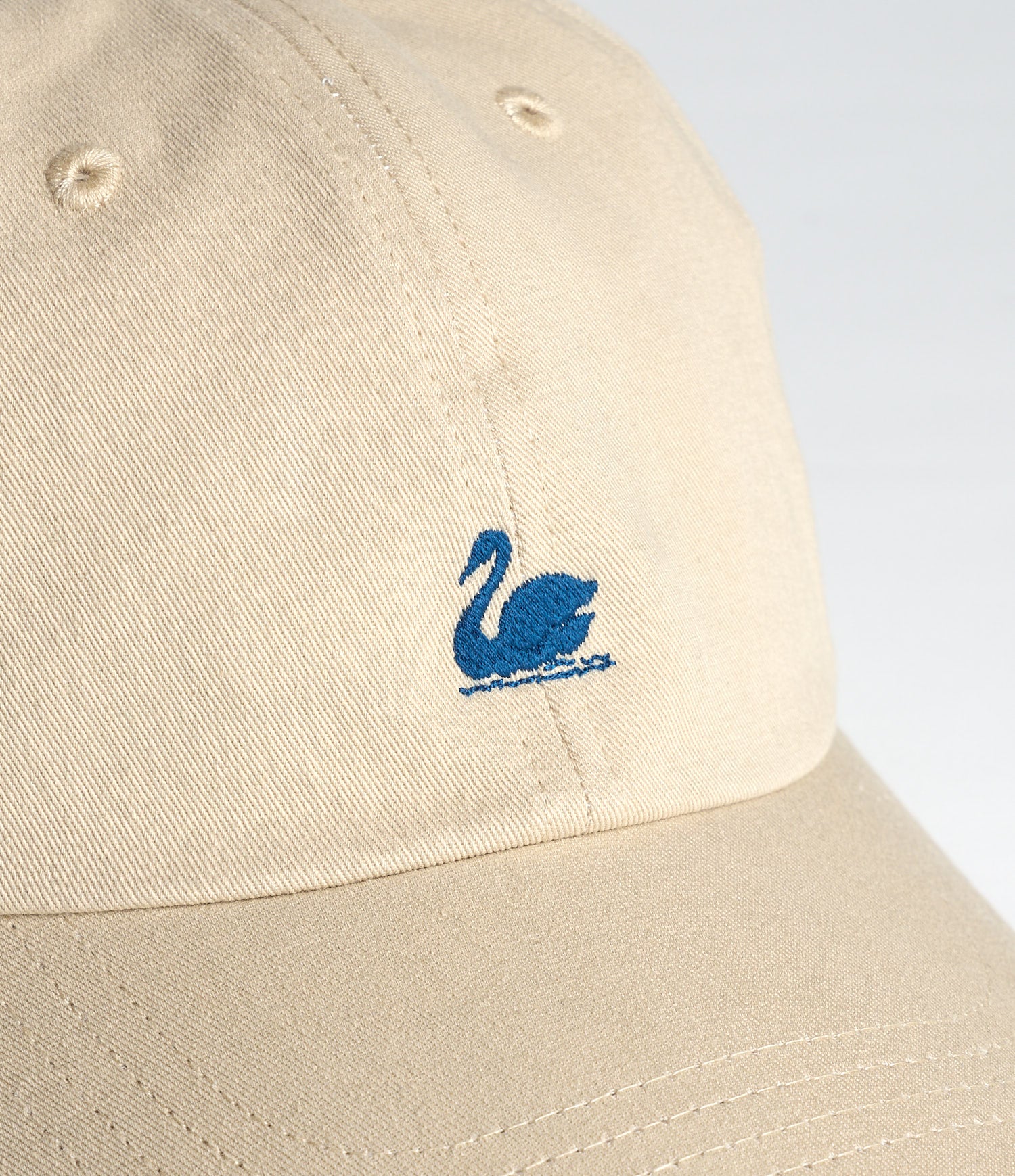Beige cap with a blue swan logo on a light gray background