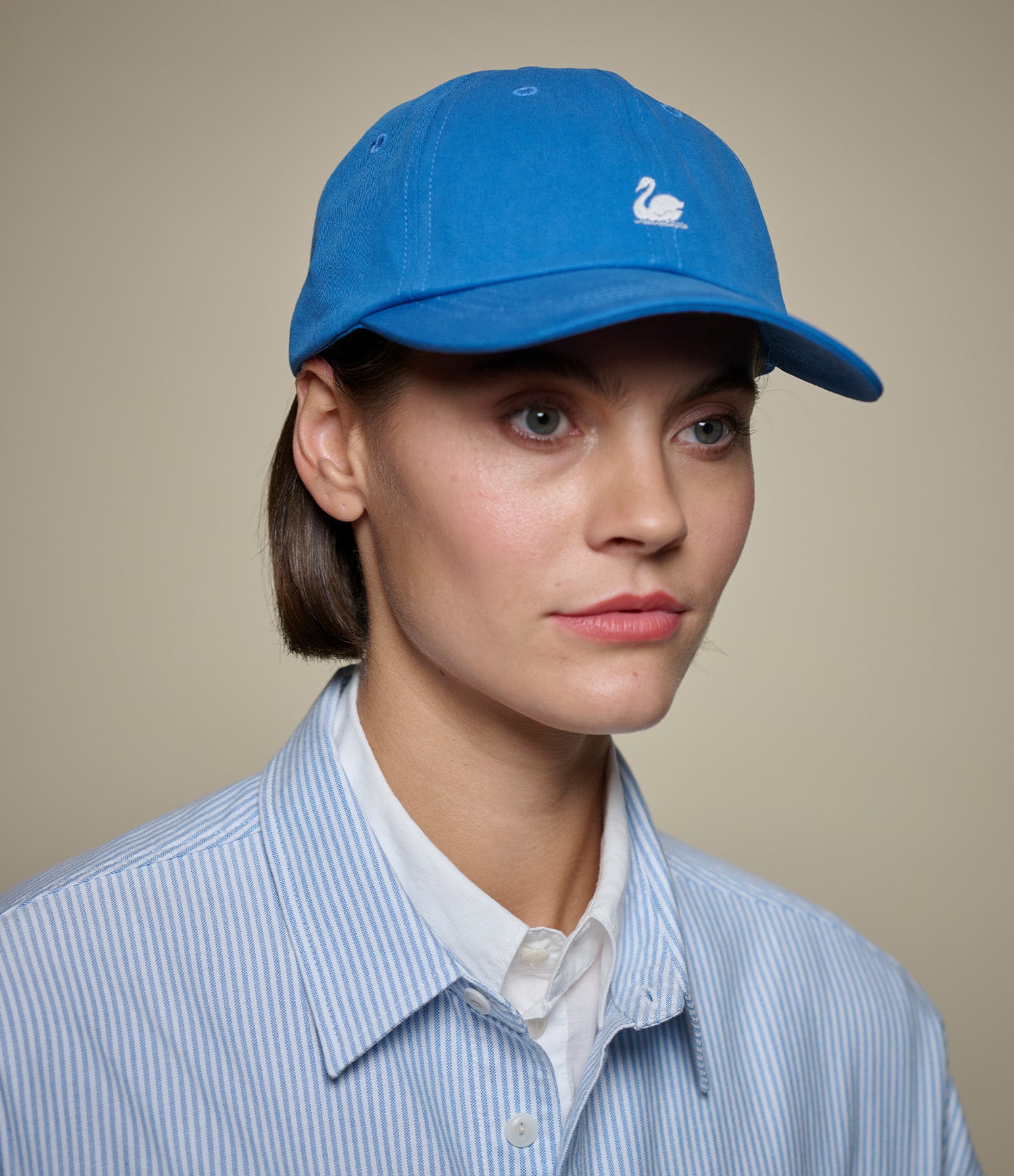 Person wearing a blue cap with a logo on a beige background