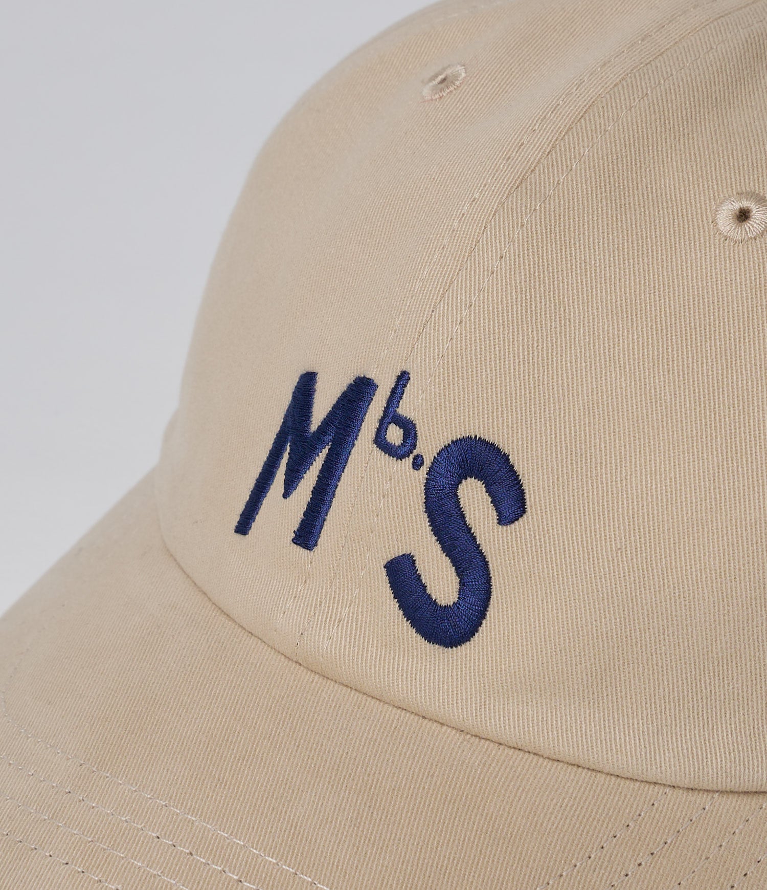 Beige cap with blue 'MbS.' embroidery on a light gray background