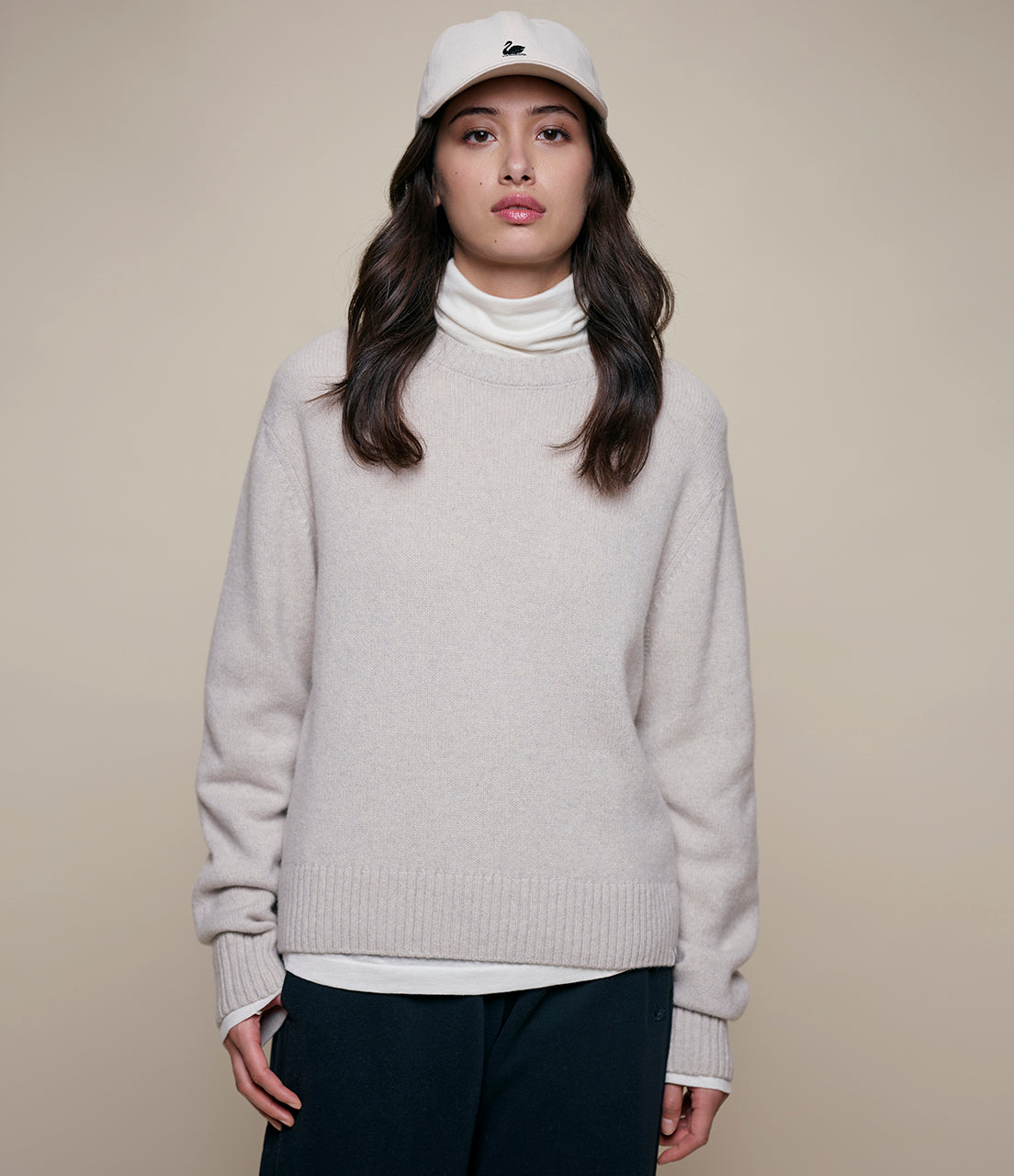 Person wearing a light gray cashmere sweater over a white turtleneck with a beige background