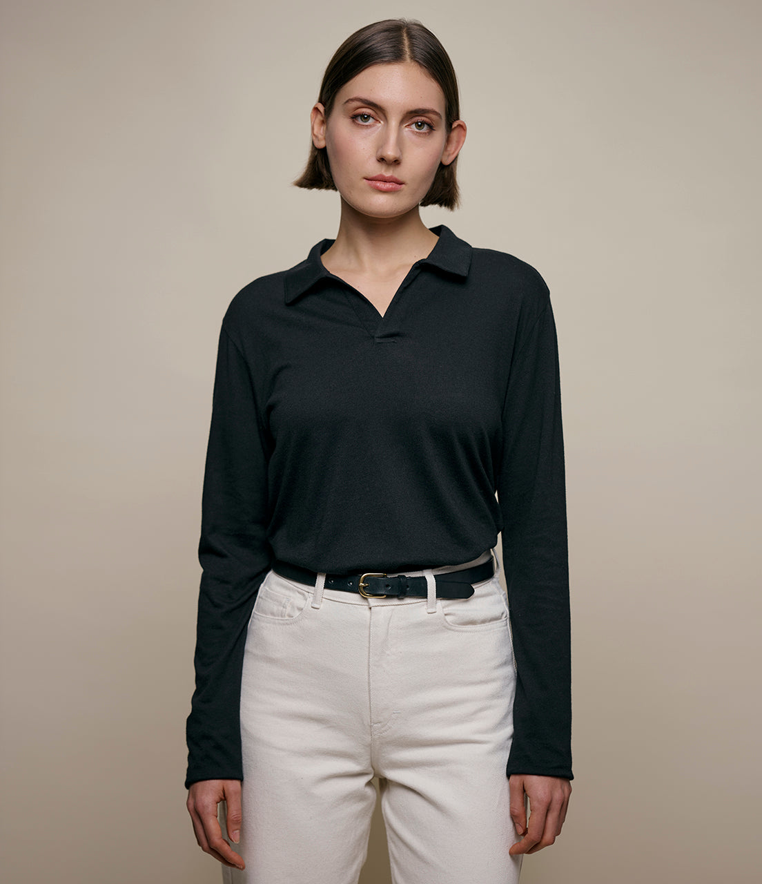Woman wearing a black cashmere long-sleeve polo shirt and white pants against a beige background