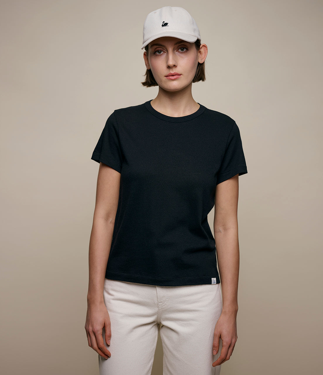 Person wearing a black cashmere t-shirt and white cap on a beige background