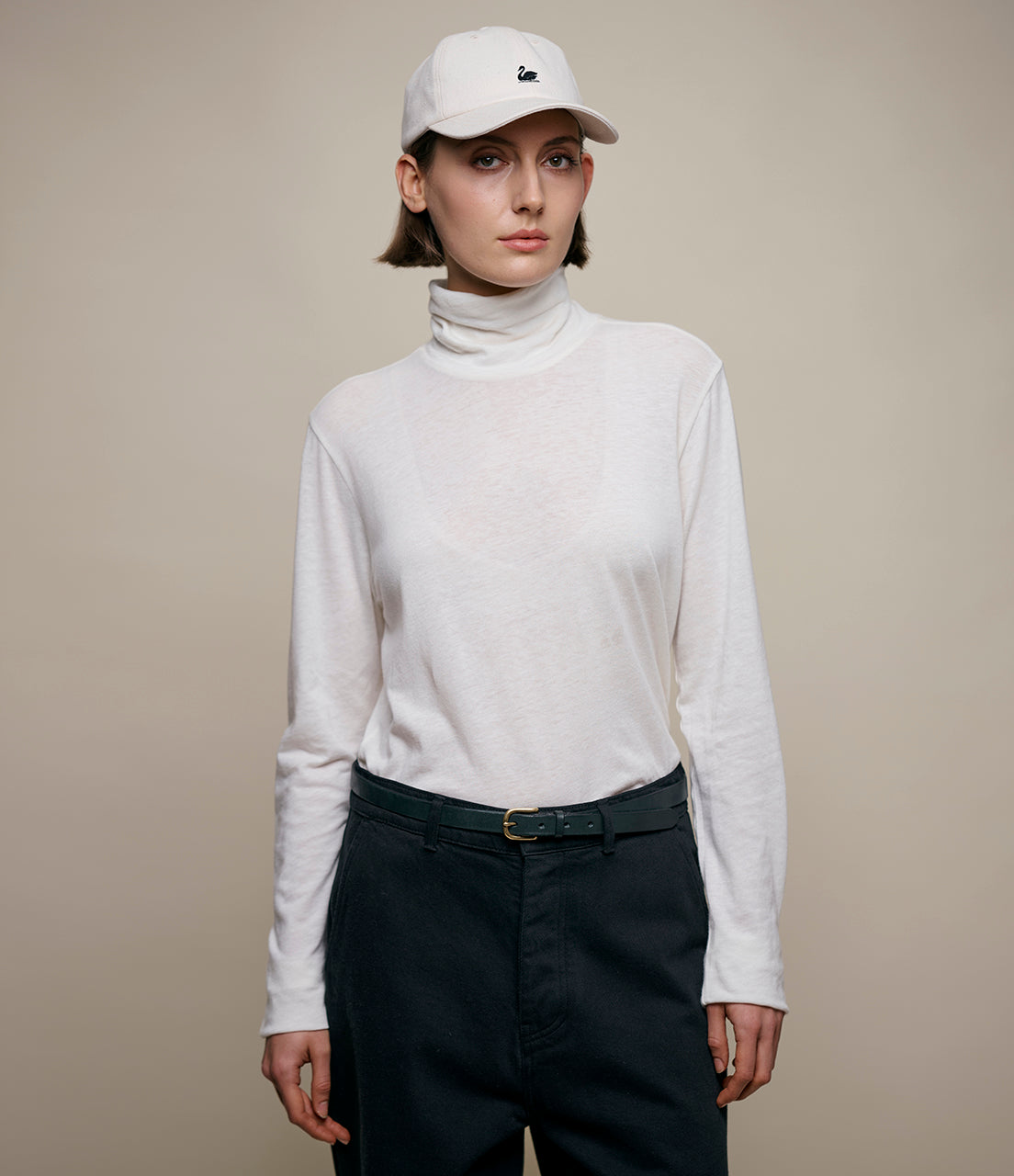 Person wearing a white turtleneck and black pants with a beige background